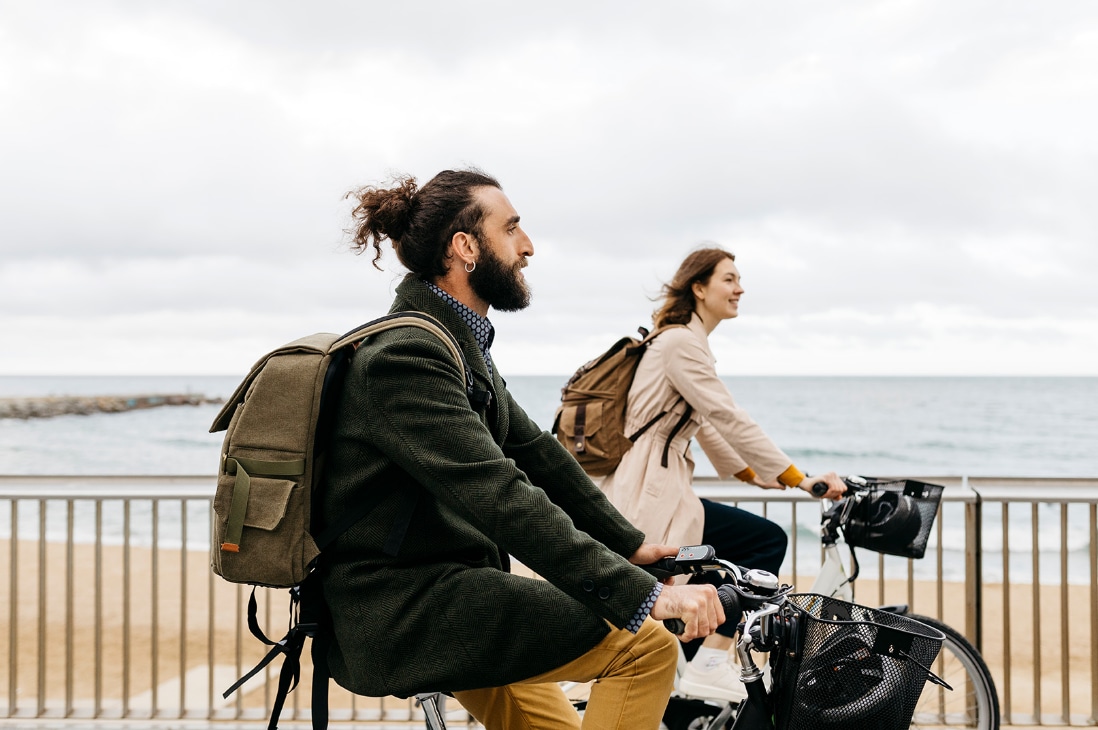 Homem e mulher em roupas de frio, com mochilas nas costas, andando de bicicleta lado a lado