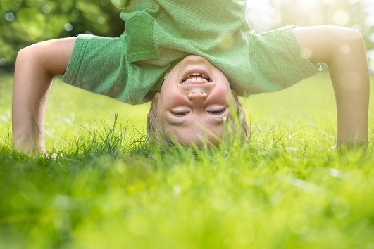 Young boy doing a headstand on the grass in the summer sunshine