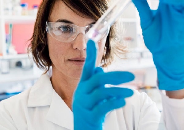 A photo of serious chemist analyzing chemical in test tube. Concentrated female scientist wearing protective eyeglasses and lab coat. She is working in laboratory.