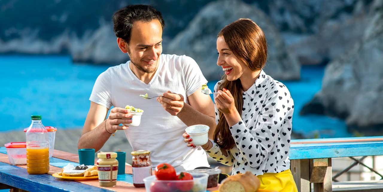 Young couple eating breakfast on the table near the sea on their summer vacation