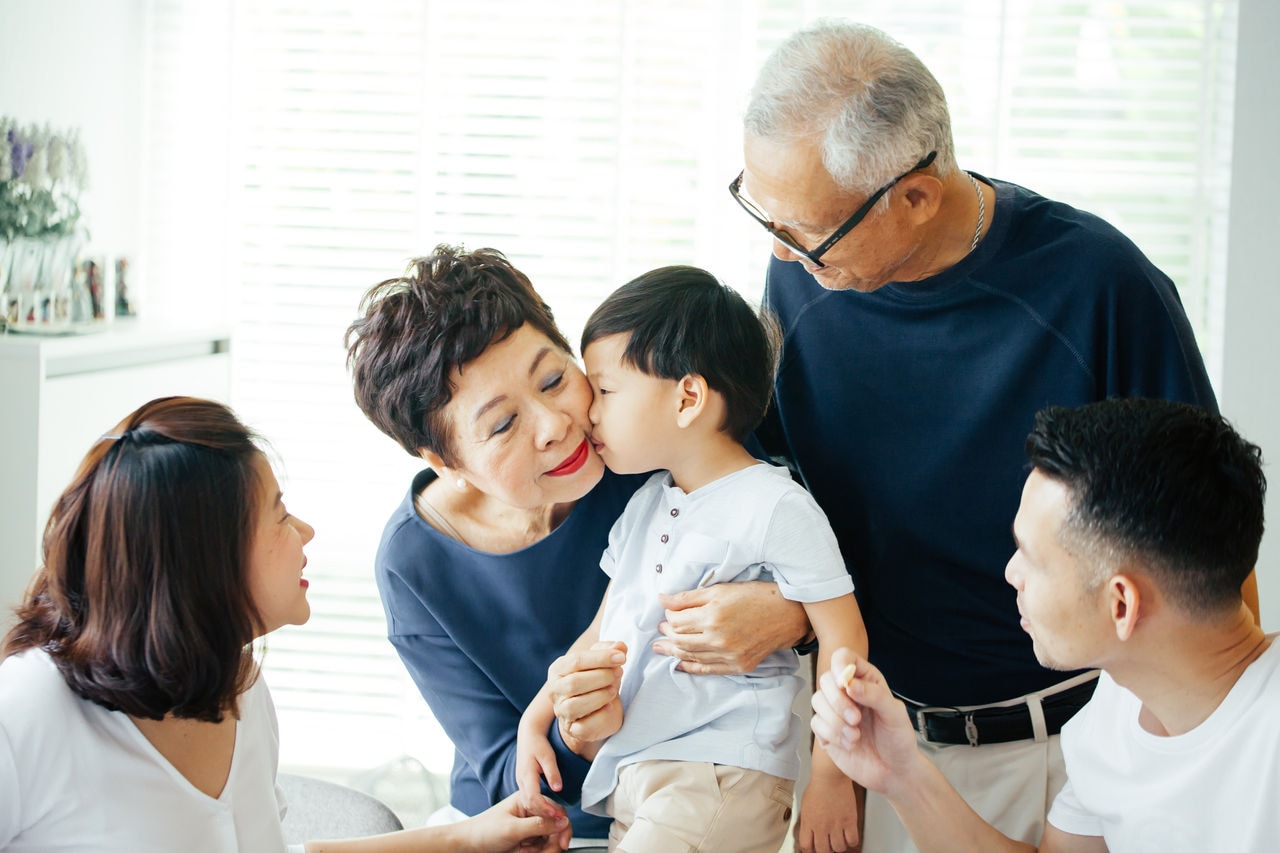 Boy kissing grandmother on cheeks with the whole Asian family of three generations together at home