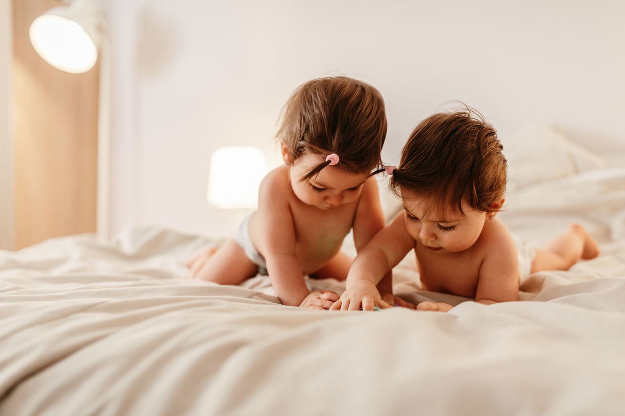 Two baby girls lying on the bed , looking at a mobile phone