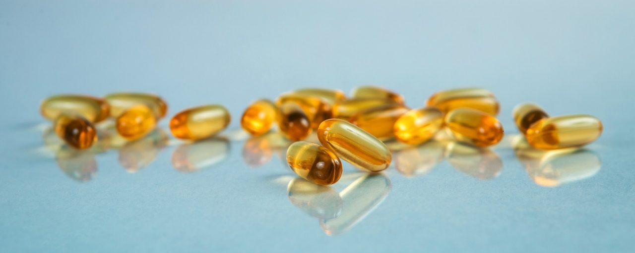 Two capsules Omega 3 on blue background and many other of capsules on blurred background.