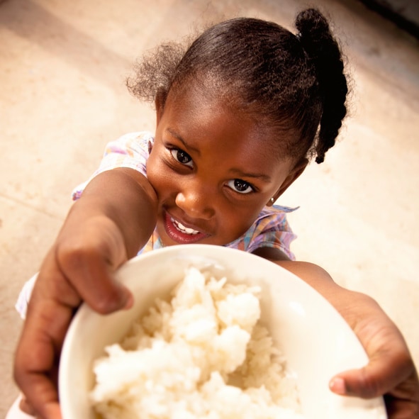 Adorable preschool age African American girl smiles while holding a bowl filled with white rice.