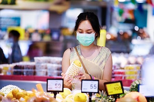 asian woman in medical face mask chooses fruits while shopping in supermarket. covid-19 spreading outbreak