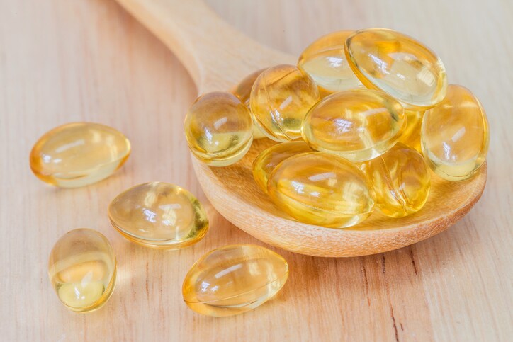 Fish oil supplement capsule, source of omega-3 on wooden spoon and natural wooden background