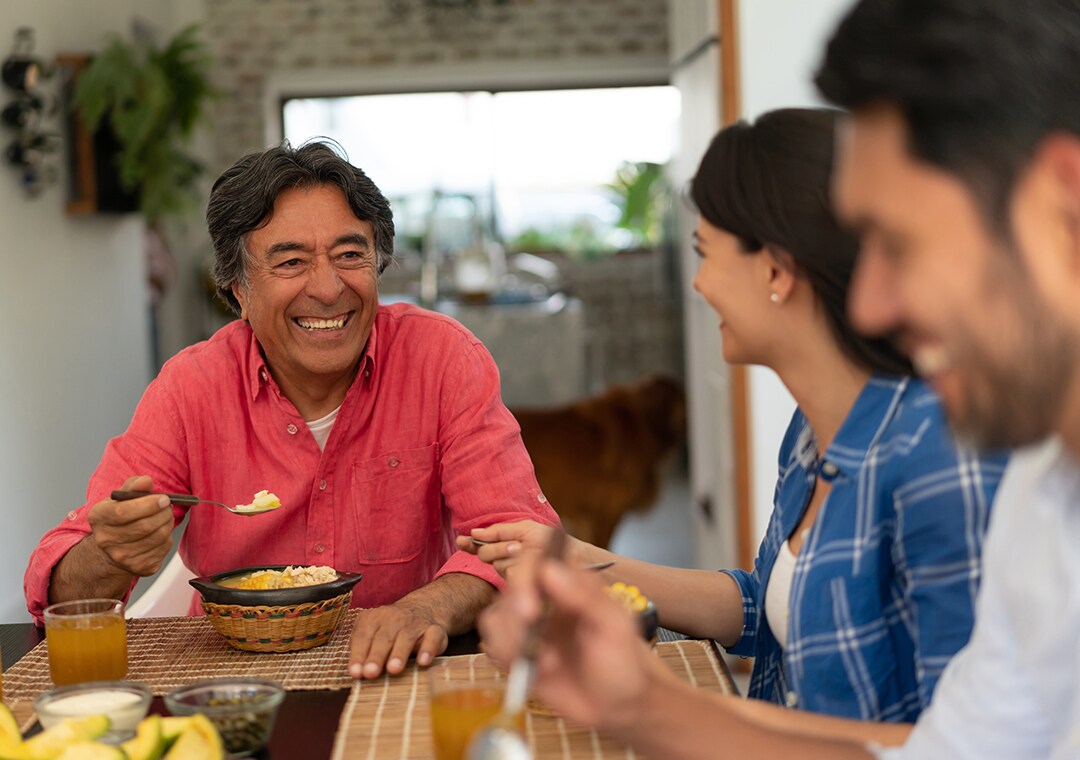 Latin american senior man with his family enjoying a delicious ajiaco all talking and smiling very happy