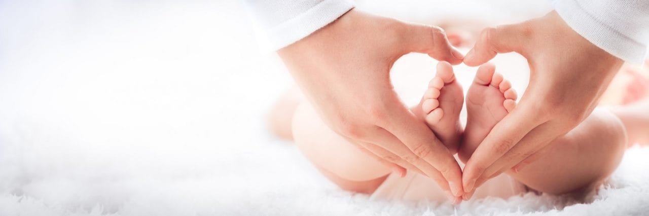 Mother Holding Baby's Feet In Heart Shaped Hands - Infant Care Concept