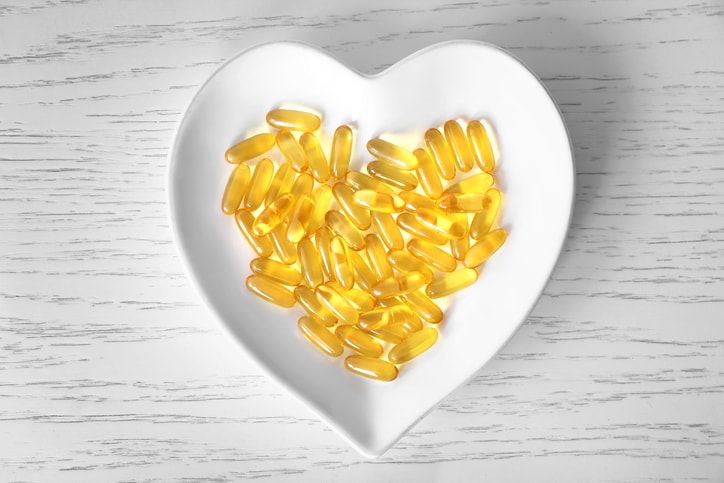 Heart-shape plate with fish oil capsules on wooden background