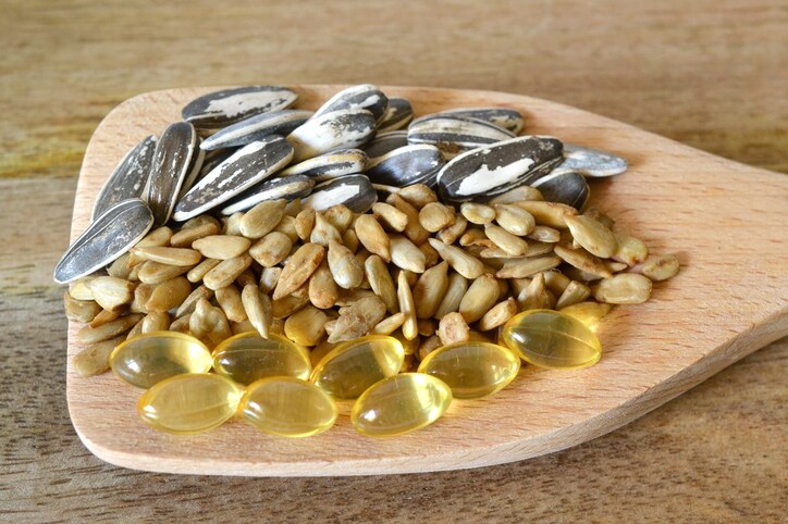 Unshelled and roasted Sunflower Seeds, and vitamin E supplements (Macro Shot on white background) on wooden spoon