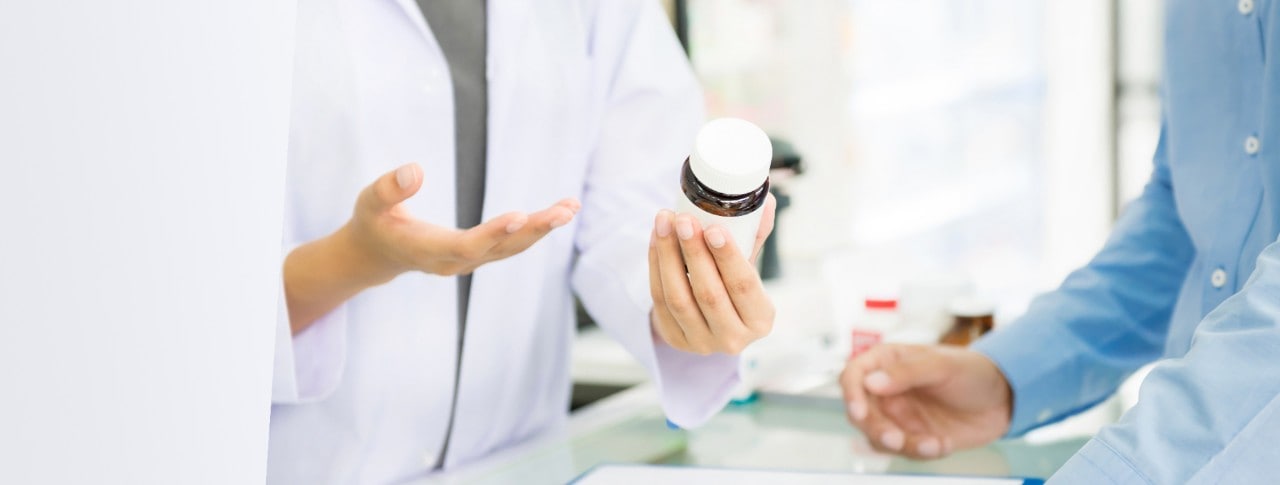 Female pharmacist holding medicine bottle giving advice to customer in chemist shop or pharmacy - horizontal web banner with copy space on the left