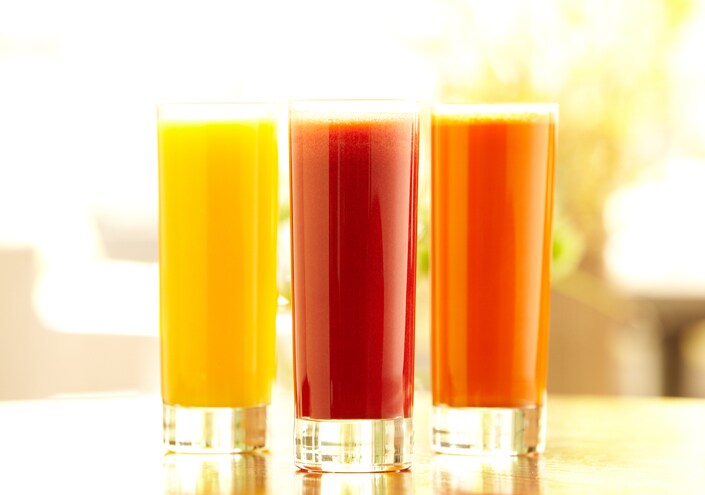 Bright still life shot of three types of juice: orange, carrot and vegetable in tall glasses sitting on a bar counter in a restaurant.  Horizontal shot.