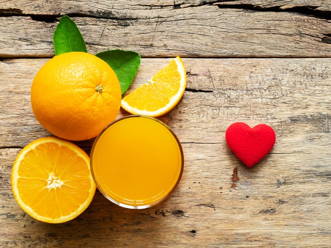 a glass of fresh orange juice and group of fresh orange fruits with green leaves, on wooden background with red heart shape. vitamin C and fruit product display or montage, studio shot