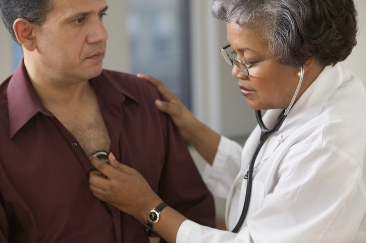 Mature female doctor listening to heart of male patient