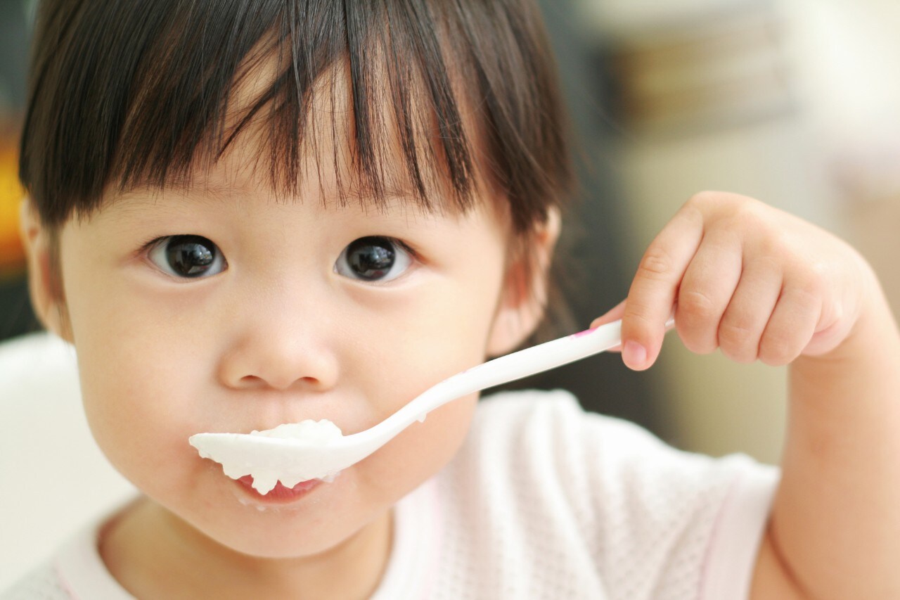 Asian toddler girl feeding herself with porridge