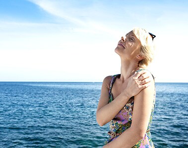Foto de uma mulher tomando sol, com o mar ao fundo