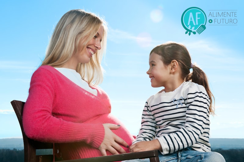 Foto de una mujer embarazada con una niña sentada en su falda.