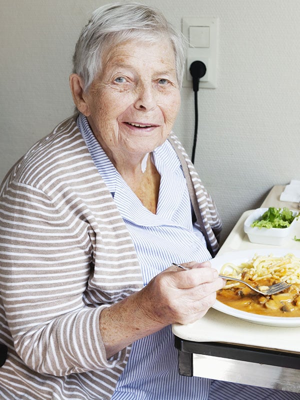Mulher idosa comendo e olhando para a câmera
