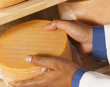 Foto de dos manos sujetando una pieza de queso envasado.