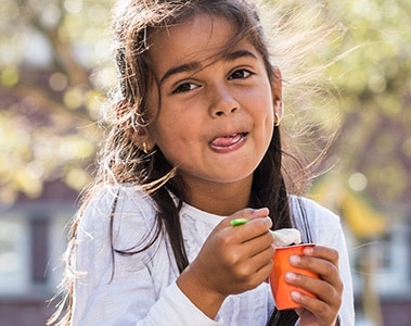 Foto de una niña sosteniendo una taza de yogur y una cuchara.