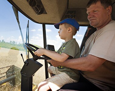 Foto de um homem, com um menino no colo, dirigindo uma colheitadeira.
