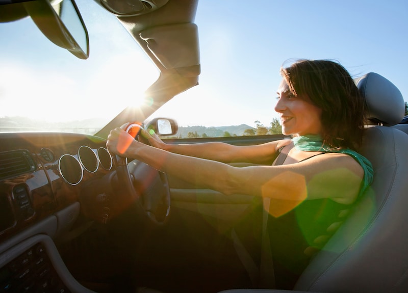 Foto de uma mulher dirigindo um automóvel conversível.