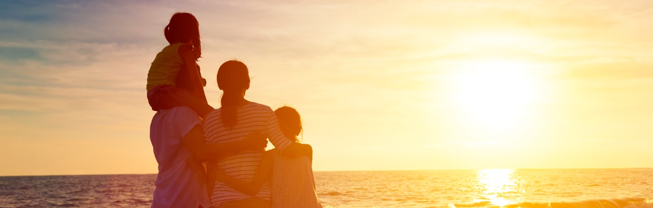 Foto de um homem, uma mulher, uma menina e um menino na praia, observando o nascer do sol.