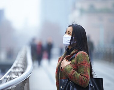 Foto de uma mulher com máscara parada em uma calçada.