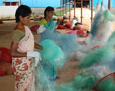 Foto de duas mulheres limpando redes de pesca.