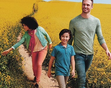 Foto de um homem, uma mulher e um menino caminhando em meio a uma plantação.